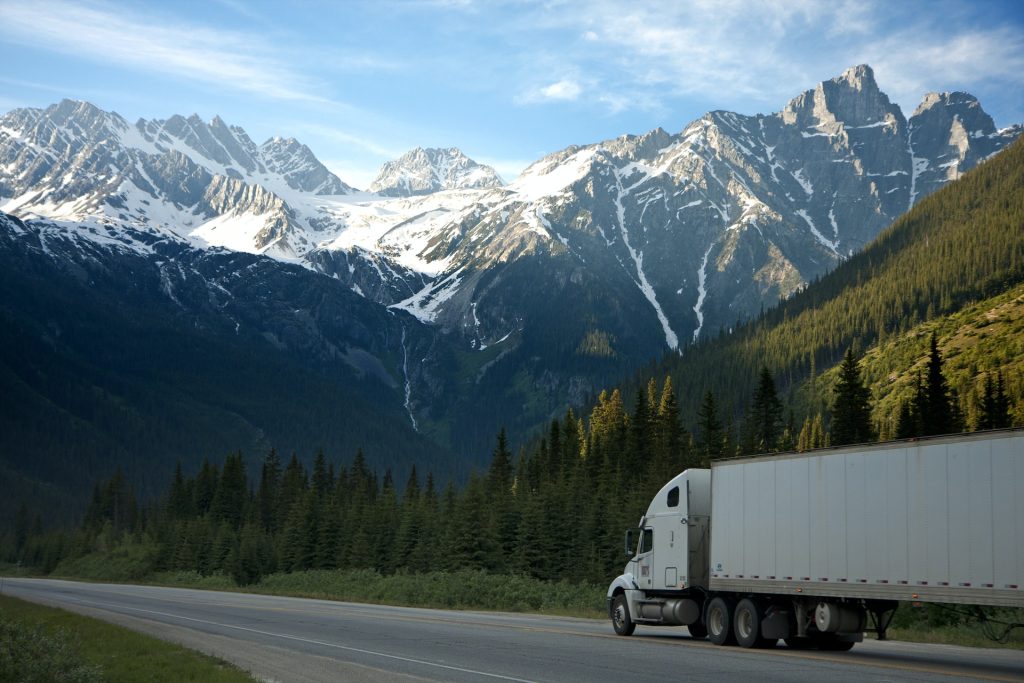 semi-truck driving on highway surrounded by pine trees and mountains
